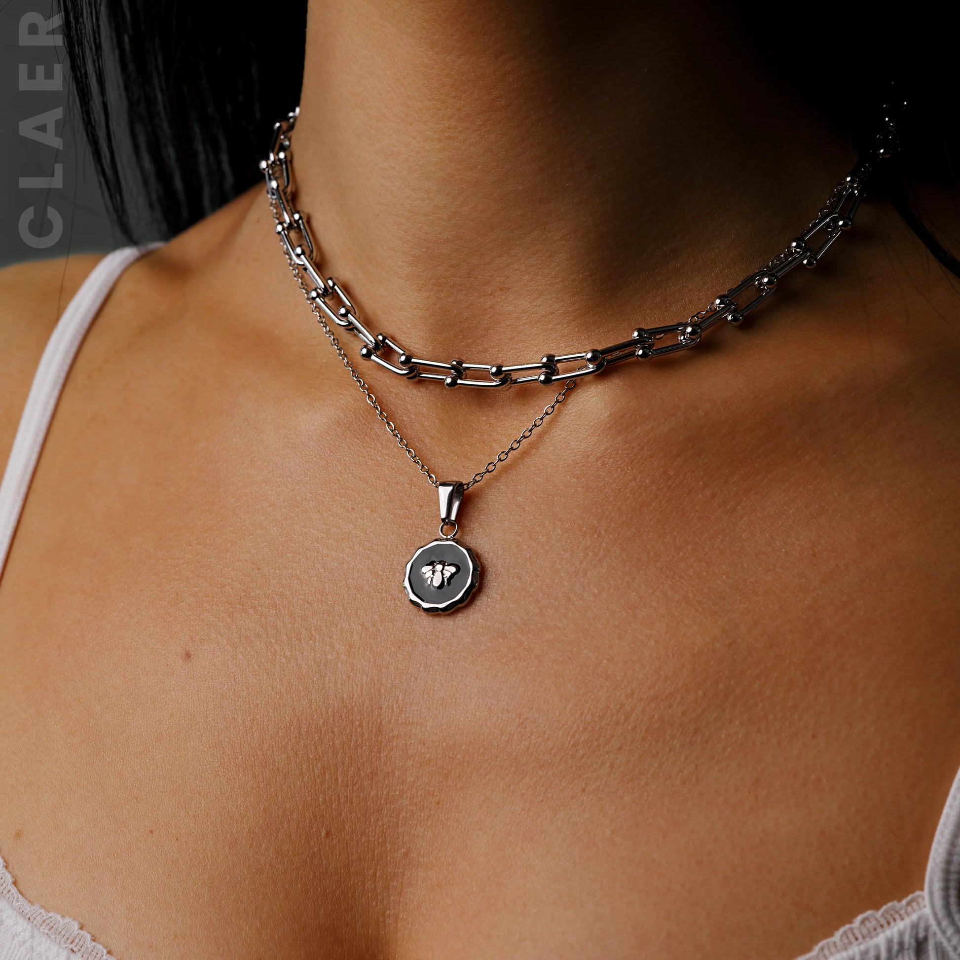 Silberne Horseshoe-Kette und Gliederkette mit einem Bienen-Charm, getragen.