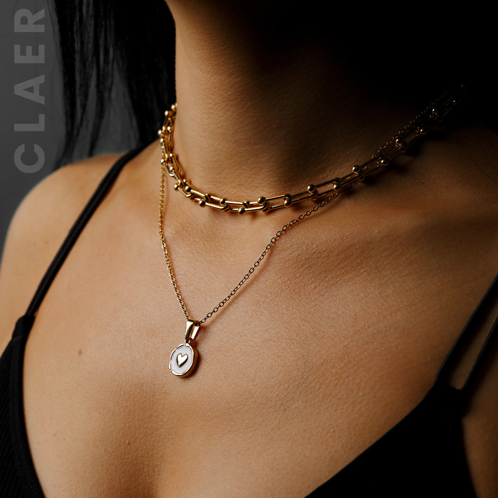 Goldene Horseshoe-Kette und Gliederkette mit einem Herz Charm, getragen.