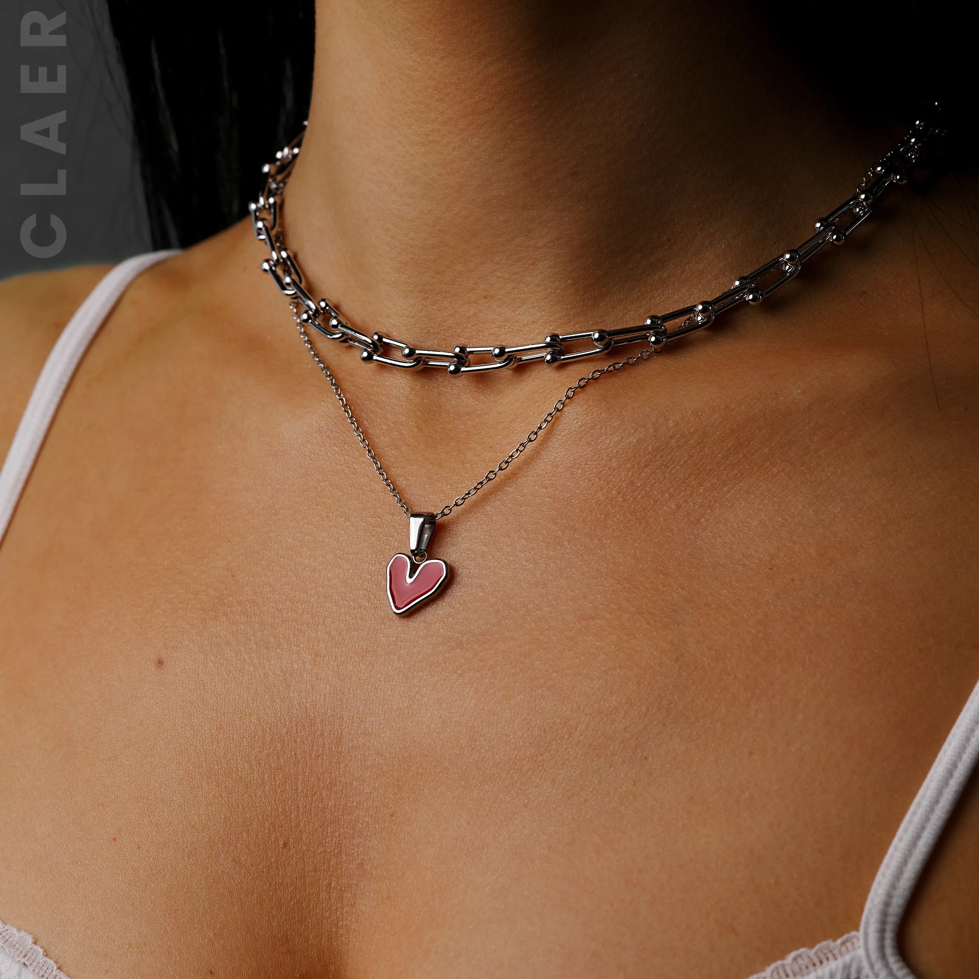 Silberne Horseshoe-Kette und Gliederkette mit einem unregelmässigem Herzanhänger, getragen.