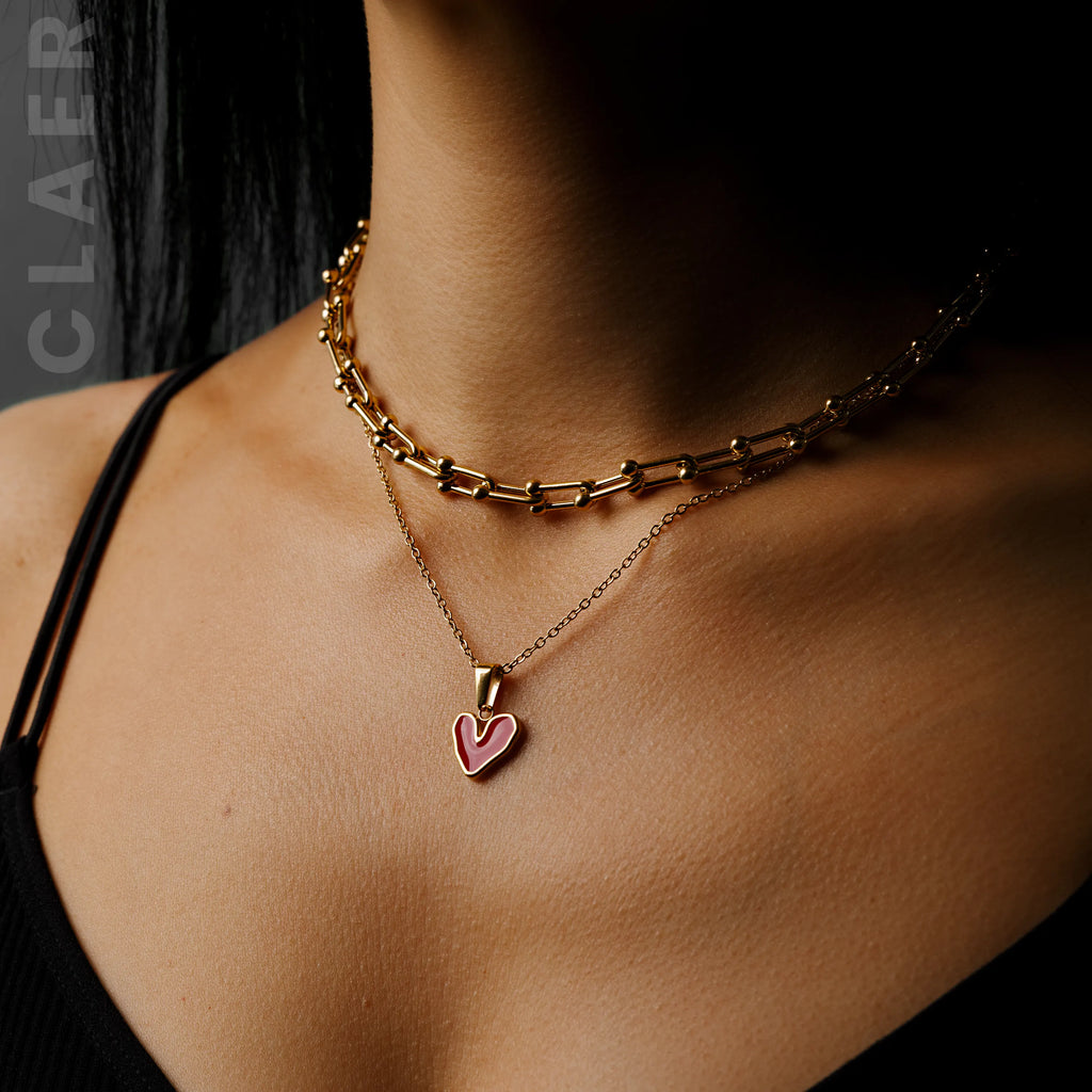 Goldene Horseshoe-Kette und Gliederkette mit einem unregelmässigem Herzanhänger, getragen.